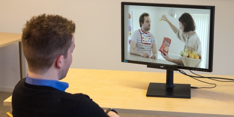 A man watching a TV commercial on a screen with Tobii Pro X2-30 eye tracker mounted on it.